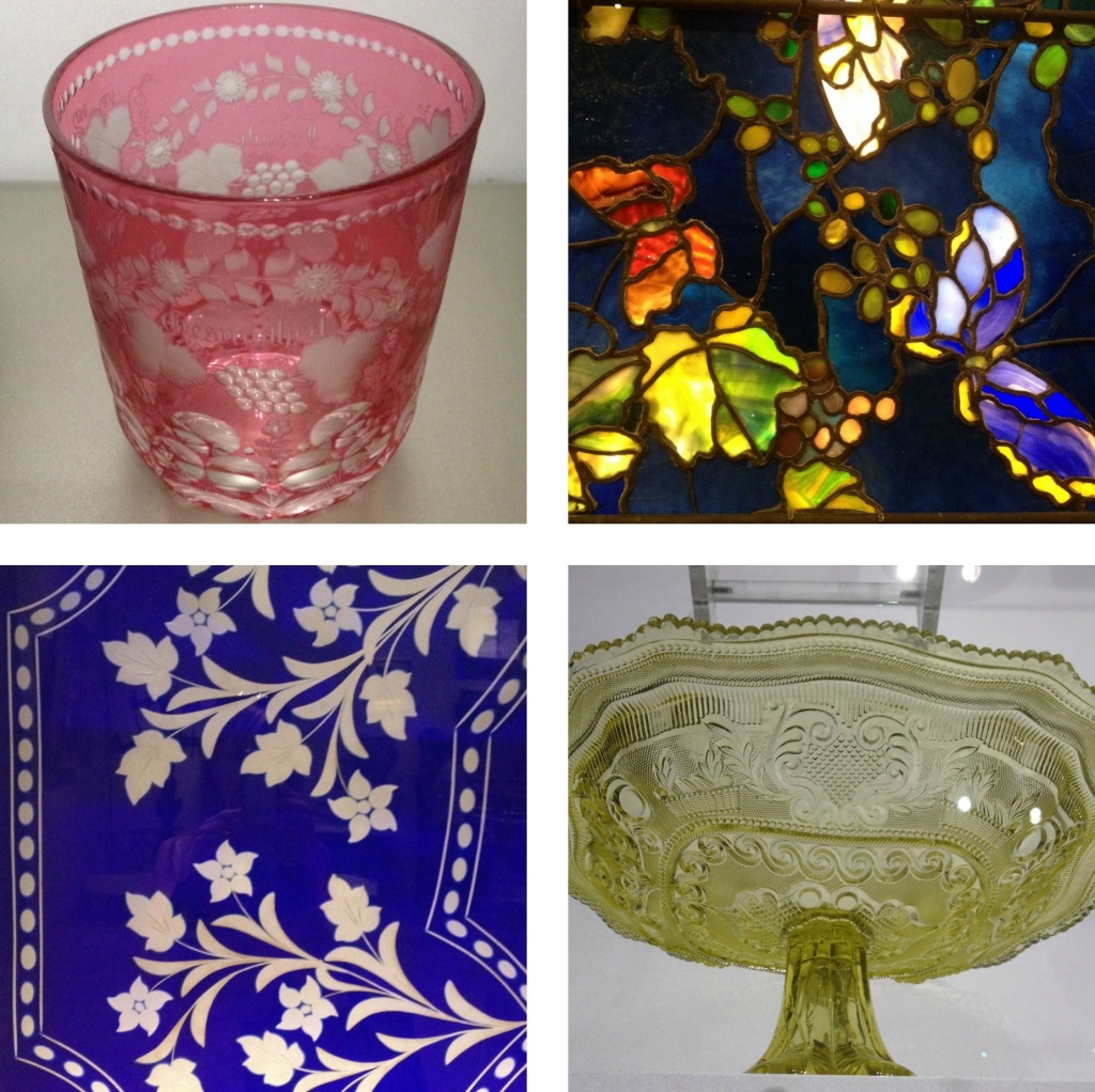 Four pieces of glass art work: a pink etched tumbler, a dark blue stained glass window with leaves and a butterfly, a royal blue glass panel etched with a flower pattern, and a pale green serving dish. 